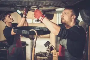 Zwei Mechaniker bei einem Ölwechsel in einer Kfz-Werkstatt – Betriebe wie dieser benötigen einen Koaleszenzabscheider für das anfallende ölhaltige Abwasser.